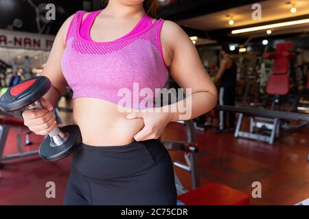 Fat woman holding dumbbell and excessive fat belly, overweight fatty belly at fitness gym. Diet lifestyle, weight loss, stomach muscle, healthy concep Stock Photo