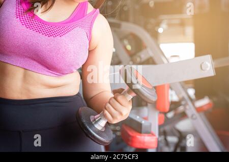 Fat woman holding dumbbell and excessive fat belly, overweight fatty belly at fitness gym. Diet lifestyle, weight loss, stomach muscle, healthy concep Stock Photo