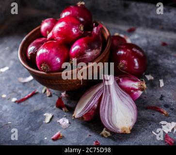A bunch of red onions in a clay bowl. Cut onion in half on a gray texture board. Stock Photo