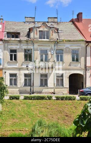 Old destroyed tenement house with broken windows among new houses. Summer. Stock Photo