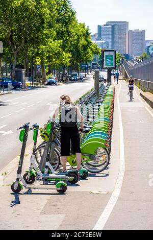 A woman is picking up a Velib shared bike in a row of bicycles lined up neatly at a docking station in Paris, along with Lime electric scooters. Stock Photo