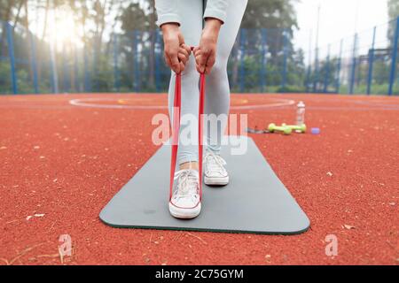 Concept of sports training outdoors. Cropped shot of female legs and hands, doing exercises for the arms and legs using fitness gum. Strengthens the Stock Photo