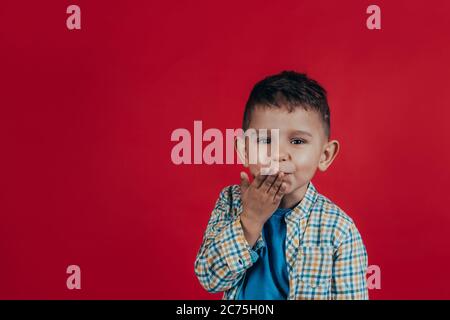 Photo of a charming boy who looks into the camera, smiles and sends a kiss on a red background Stock Photo