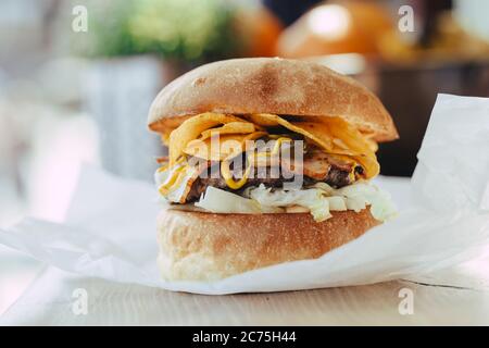 Fresh homemade burger close-up with cutlet, bacon, chips and mustard sauce on a wooden table. Stock Photo