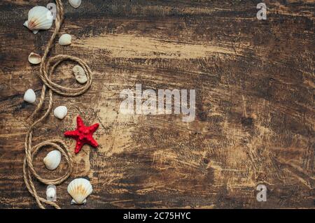 Summer time, sea vacation. Red starfish, rope and seashells on dark wooden with place for text. Stock Photo