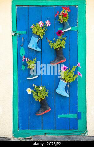 Old children rubber boots with blooming summer flowers on the entrance door of a house Stock Photo