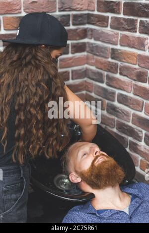 Barber woman washes customer man head. Concept barbershop. Stock Photo