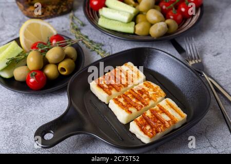 Grilled haloumi cheese on a black pan with olives, tomatoes, cucumbers and pepperoni. Close-up. Stock Photo