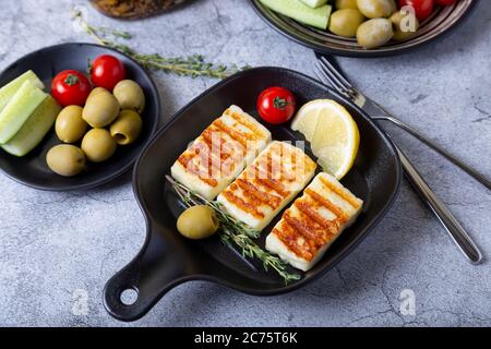 Grilled haloumi cheese on a black pan with olives, tomatoes, cucumbers and pepperoni. Close-up. Stock Photo