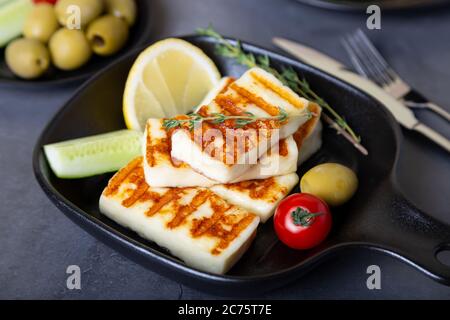 Grilled haloumi cheese on a black pan with olives, tomatoes, cucumbers and pepperoni. Close-up. Stock Photo