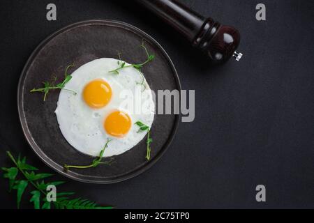 Breakfast with two fried eggs and herbs on black background Stock Photo