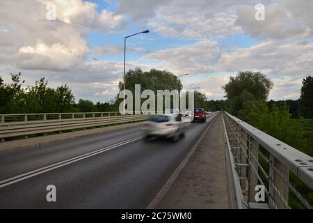 Blurry silhouettes of cars on the bridge against the background of clouds in the blue sky. Summer. Stock Photo