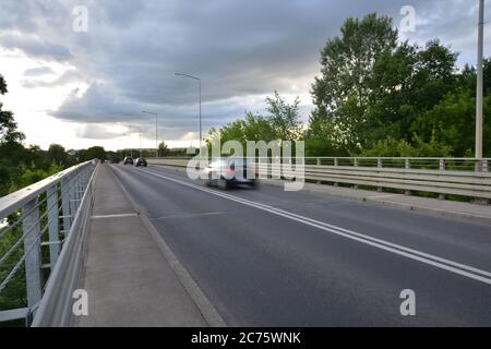 Blurry silhouettes of cars on the bridge against the background of clouds in the blue sky. Summer. Stock Photo