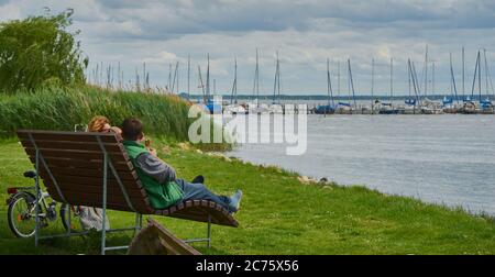 Steinhude, Germany, June 7., 2020: Couple relaxing on a bench eating ice cream and enjoying the view of the lake Stock Photo