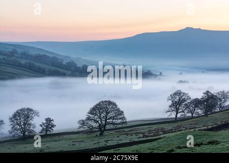 Simons Seat towers above the landscape of Wharfedale near Appletreewick on a misty winter morning as a temperature inversion fills the valley. Stock Photo
