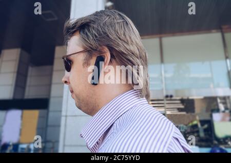 walking  in the city blond man in sunglasses with handsfree headset Stock Photo