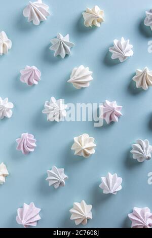 Pattern with delicate light green, white, yellow and pink meringue cookies. Meringues are lying in rows on blue paper background. Unhealthy food conce