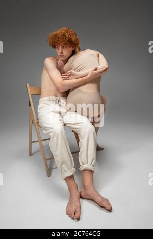 Hiding. Fashion portrait of beautiful redhead couple isolated on grey studio background. Concept of beauty, skin care, fashion and style. Artwork, modern and trendy portrait. Attractive model. Stock Photo