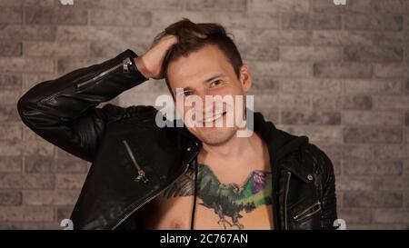 A man in a fancy jacket with a tattoo on his chest. Portrait of a young man in a leather jacket, smiling at the camera on a white background Stock Photo