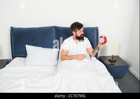Morning again. Stressful man wake up turn off alarm clock. Time to wakeup. Unhappy handsome man in bed. Man suffering on mornings. Terrible noise. Insomnia and sleep disorder. Daily routine. Stock Photo