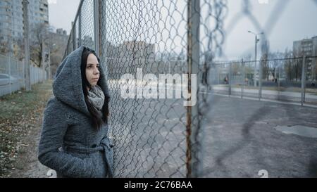 A young beautiful woman in the gray coat poses near a lattice fence in a late autumn. Stock Photo