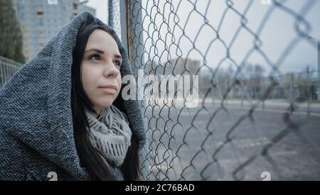 A young beautiful woman in the gray coat poses near a lattice fence in a late autumn. Stock Photo