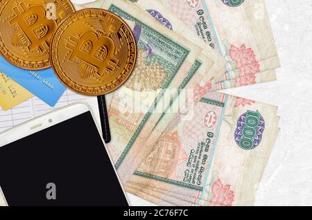 1000 Sri Lankan rupees bills and golden bitcoins with smartphone and credit cards. Cryptocurrency investment concept. Crypto mining or trading transac Stock Photo