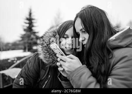 The meeting of girlfriends on street. Two women look in mobile phone, considering their photos on walk. Black and white photo. Stock Photo