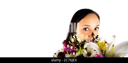 Young woman with colorful bouquet of various flowers on isolated white background. Brunette looks out from behind basket of florets. Stock Photo