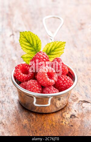 Ripe red raspberries and green leaves on wooden table. Stock Photo