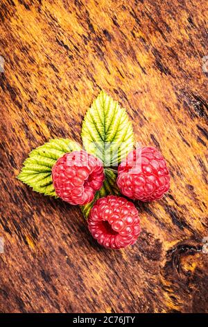 Ripe red raspberries and green leaves on wooden table. Stock Photo