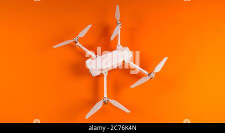 Close-up of white drone on orange background. Modern drone unmanned aerial vehicle with propellers. Stock Photo