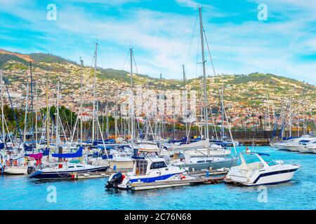 Marina with moored yachts and motorboats in evening sunlight, Funchal cityscape on mountains in background, Madeira island, Portugal Stock Photo