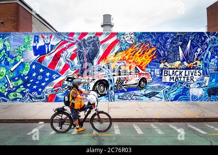 Brooklyn, New York, USA - June 27, 2020: Bicycle delivery man rides past Painted mural depicting the Black Lives Matter and covid-19 in New York. Stock Photo