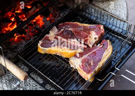Close-up three big tasty juice raw t-bone beaf steak on grill at barbecue with bright hot burning charcoal at brazier. BBQ meal cooking background Stock Photo