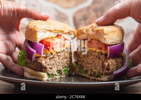 Two people's hands sharing a vegetarian burger made with beans and lentils Stock Photo