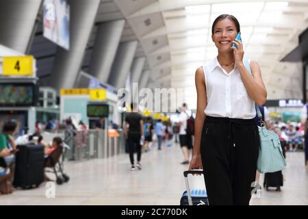 Businesswoman on commute transit talking on the smartphone while walking with hand luggage in train station or airpot going to boarding gate. Asian Stock Photo