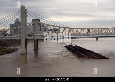 A barge hauling a cargo of coal upstream on the Ohio River passes under the I-65 Kennedy and Lincoln bridges by downtown Louisville, Ky. Stock Photo