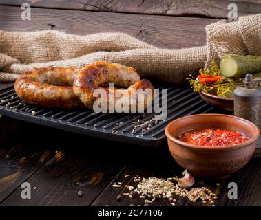 Spicy homemade sausages pork and beef sausages, on a wooden background, with sauce,  spices and pickled cucumber . Template in rustic style. Stock Photo