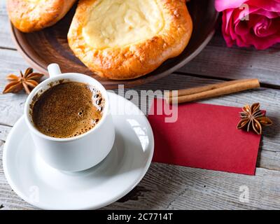 Open buns with cottage cheese (vatrushka)lying in a clay plate on a wooden table with rose and red card. Сloseup. Morning still life Stock Photo