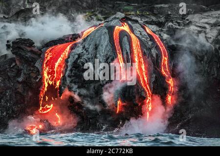 Hawaii lava flow entering the ocean on Big Island from Kilauea volcano. Volcanic eruption fissure view from water. Red molten lava Stock Photo