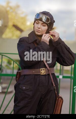 A young female pilot in uniform of Soviet Army pilots during the World War II. Black flying jumpsuit, helmet and goggles. Photo in retro style. Stock Photo