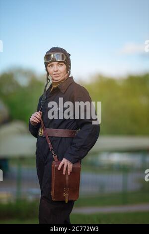 A young female pilot in uniform of Soviet Army pilots during the World War II. Black flying jumpsuit, helmet and goggles. Photo in retro style. Stock Photo