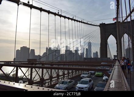 View the cables and the car deck of the Brooklyn Bridge, towards downtown New York City skyline including One World Trade Centre. People seen walking. Stock Photo