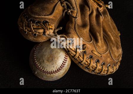 Worn out catchers mitt resting on a scuffed up stained old baseball Stock Photo