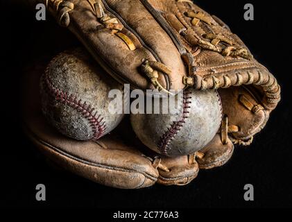 Two scuffed and worn out baseballs in an old leather glove on dark background. Stock Photo