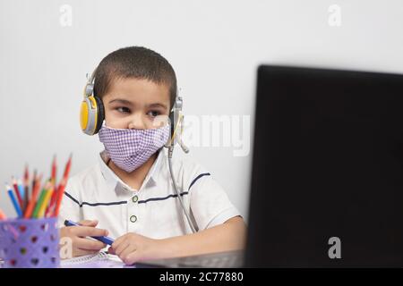 Young kid in headphones doing online exercises via laptop. Learning foreign language online or distance education, e-learning concepts Stock Photo