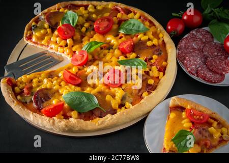 Slice of pizza with cherry and basil on a black background. Ingredients for preparing national Italian food. Tasty freshly prepared pizza with cherry Stock Photo