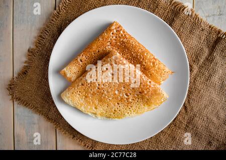 Pancakes on a white plate on a linen background. Russian traditional food crepes for the holiday Maslenitsa. Flat lay Stock Photo