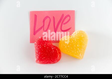 Pink sticker with the word love and two red marmalade in the shape of a heart. Symbol of love on a white background Stock Photo
